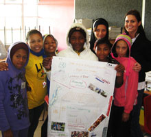Nicole Motter visiting students in Cape Town, South Africa, who are standing with her, holding a project poster about human rights. 